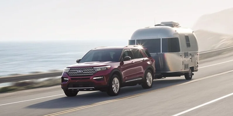 A 2024 Ford Explorer towing a caper behind it on a road near the ocean.