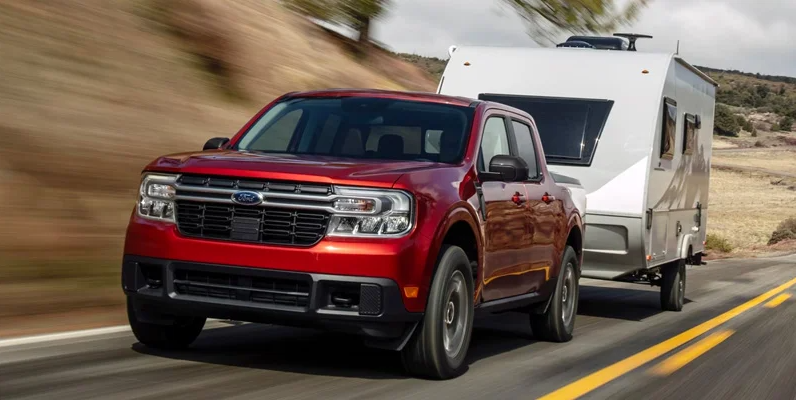 A red 2024 Ford Maverick driving down the road towing a camper.