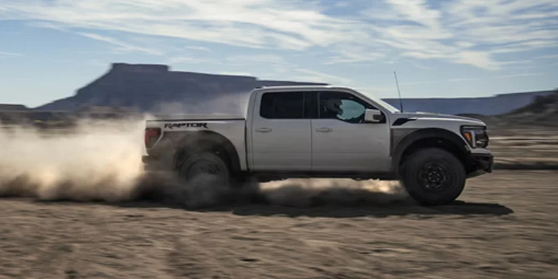 A photo of a white Ford F-150 driving through a sandy desert.