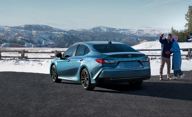 A photo of a couple taking a selfie next to a 2025 Toyota Camry with snow in the backround.